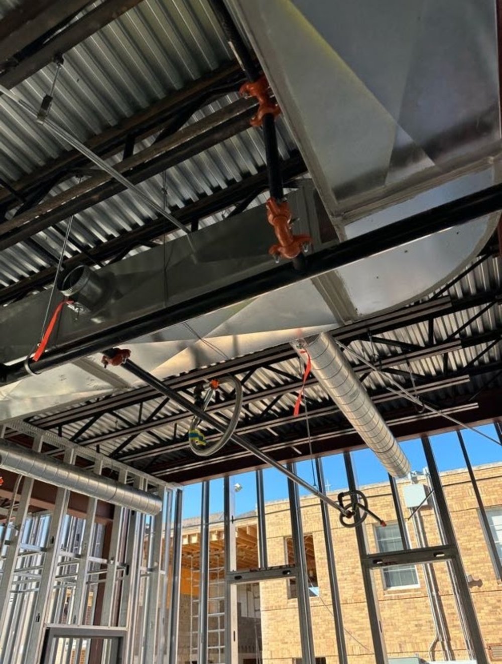 Rectangular supply duct and spiral duct hung under a steel roof deck