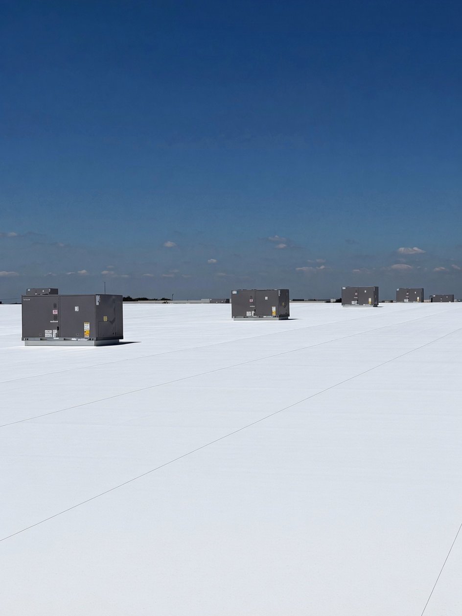 Row of rooftop HVAC units on a white commercial roof under a blue sky