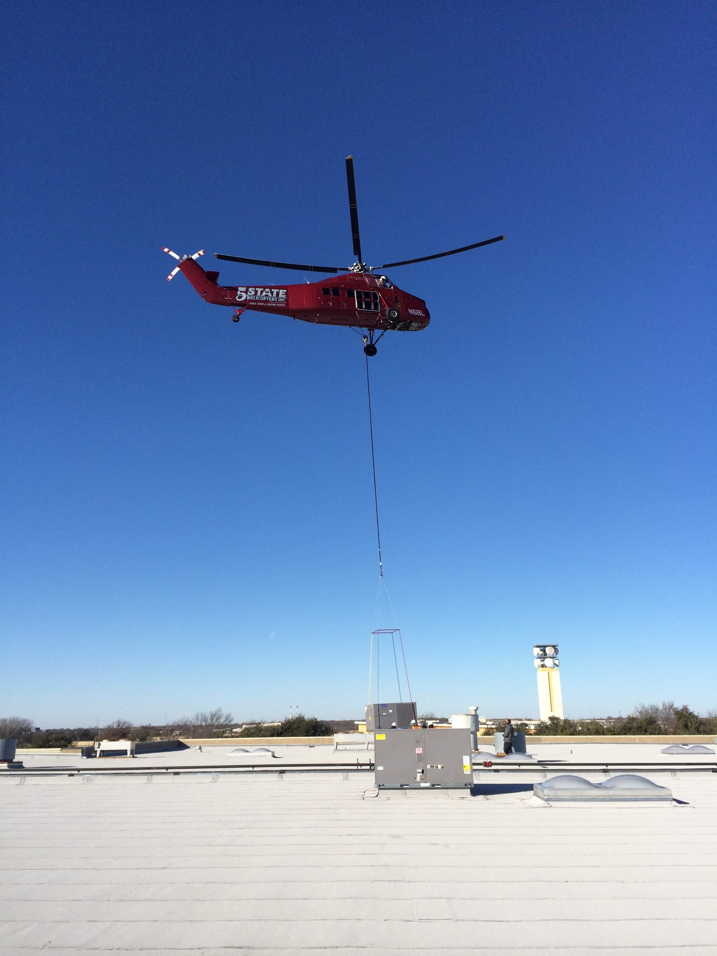 Red helicopter lifting a rooftop HVAC unit onto a commercial roof